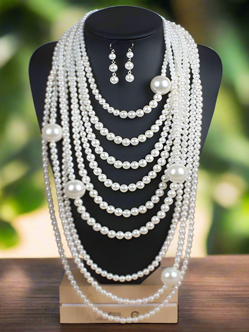 A luxurious looking multi-layered pearl necklace displayed on a black bust stand, featuring cascading strands of white pearls in varying sizes with matching pearl drop earrings.