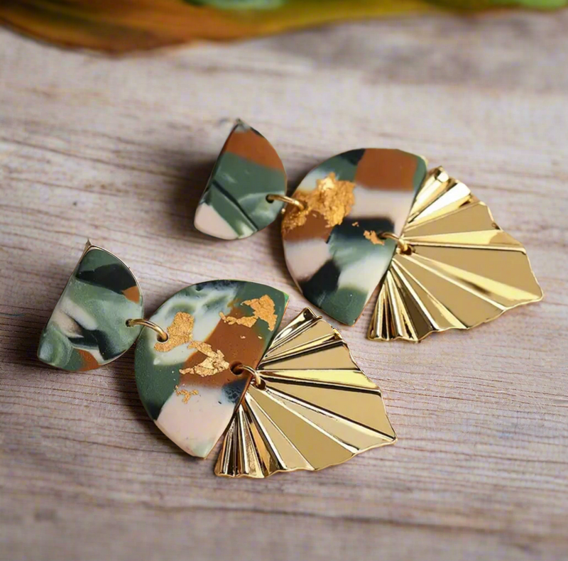 Pair of gold-tone Nala Half-Bottom Earrings with a sculpted half-fan leaf design, placed on a dark textured background.