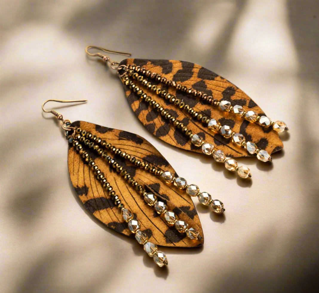Leopard-print faux leather earrings with beaded strands of gold, bronze, and crystal beads, displayed on a white surface.
