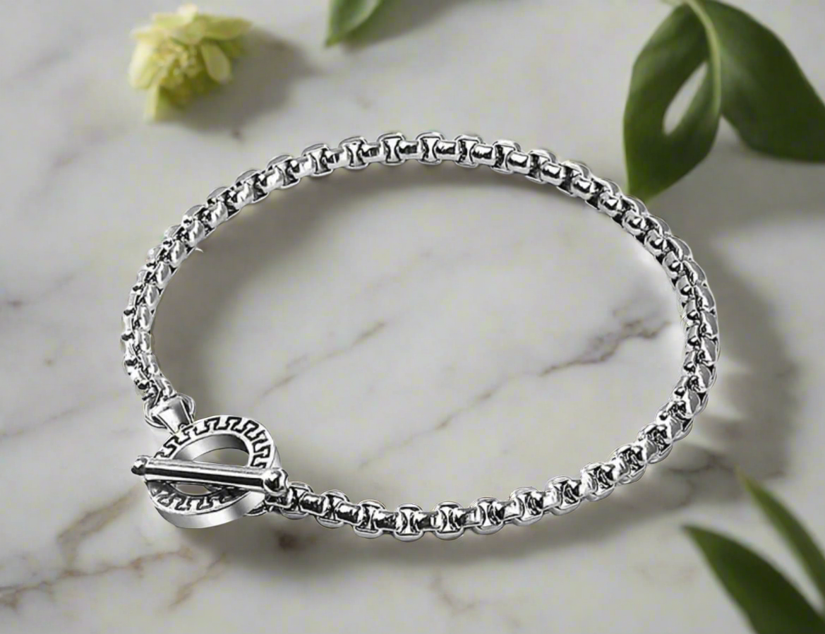 Close-up of a men’s stainless steel bracelet with a toggle clasp featuring an engraved circular design, worn on wrist.