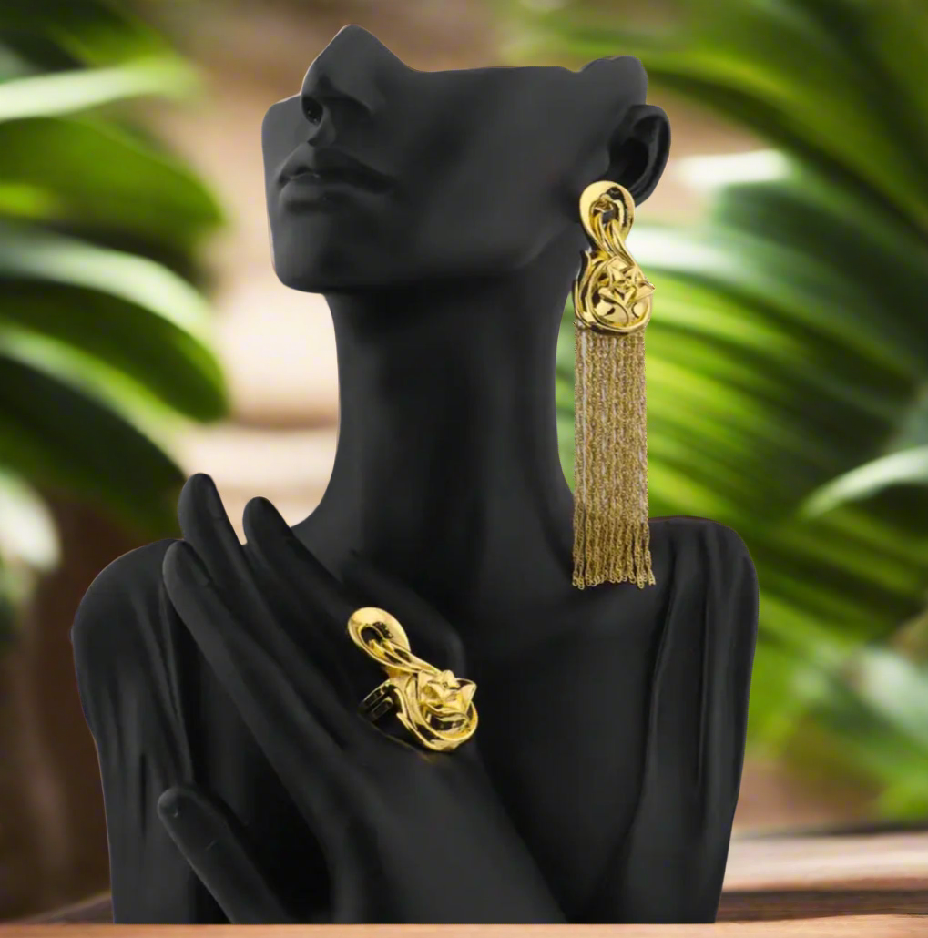 Gold Waridi tribal earrings with intricate floral design tops and long gold tassels, laid on a tropical-themed background.