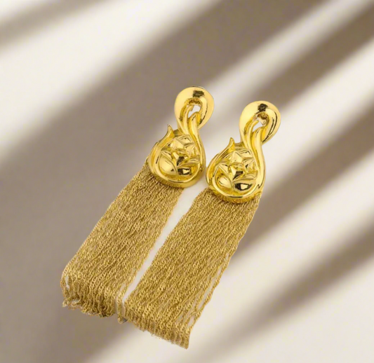 Gold Waridi tribal earrings with intricate floral design tops and long gold tassels, laid on a tropical-themed background.