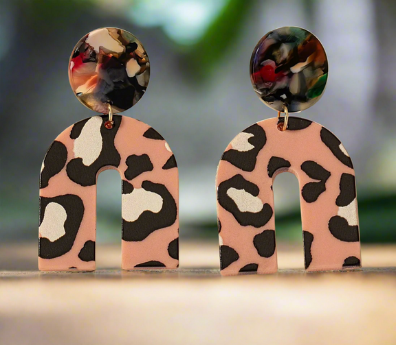 The Catalina earrings by Desiree W.A.R Store showcase a leopard print on the lower halves with vibrant, multicolored marble effect round tops, beautifully set against a light surface.