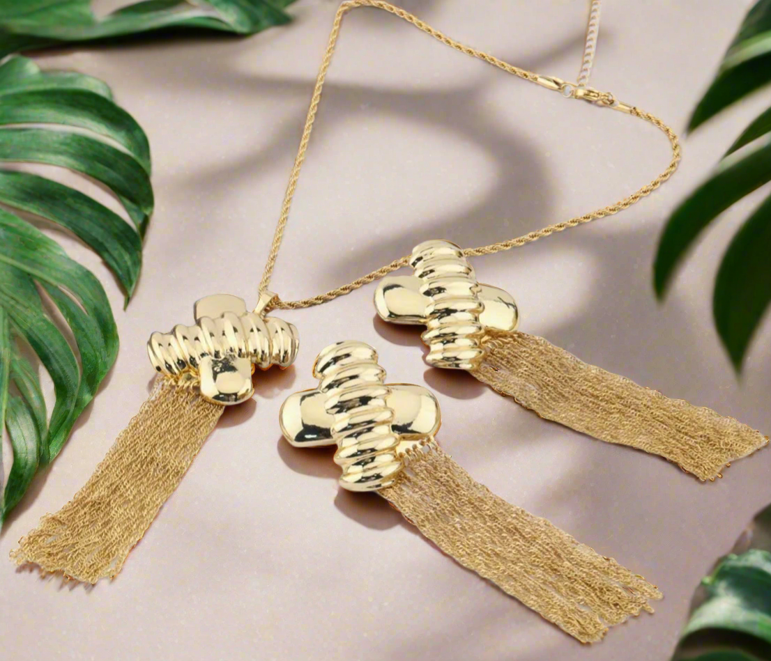Gold jewelry set with abstract hammered pendant and matching tassel earrings displayed on black bust stand