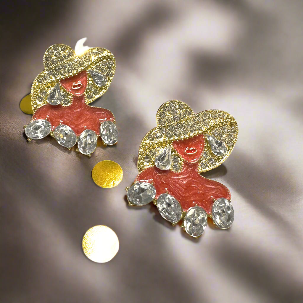 A pair of elegant gold statement earrings featuring a stylish woman in a sparkling hat with teardrop and oval-shaped crystal embellishments, displayed on a white and gold polka-dot background.