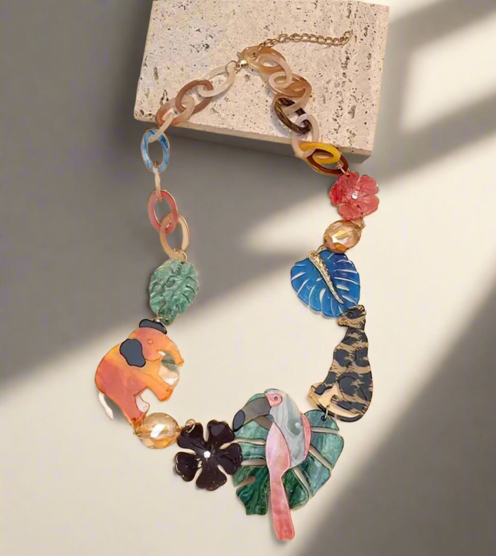Colorful jungle-themed statement necklace with resin charms of a pink flamingo, orange elephant, leopard, tropical leaves, and flowers, connected by multicolored acrylic chain links.
