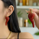 Glossy red chili pepper-shaped stud earrings with gold-tone stems on a white background.
