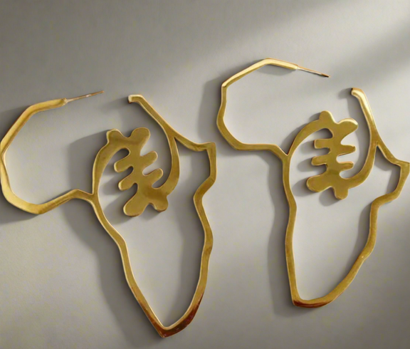 A pair of gold earrings shaped like the African continent, featuring a bold, intricate central design and smooth golden edges, displayed against a soft, neutral background.