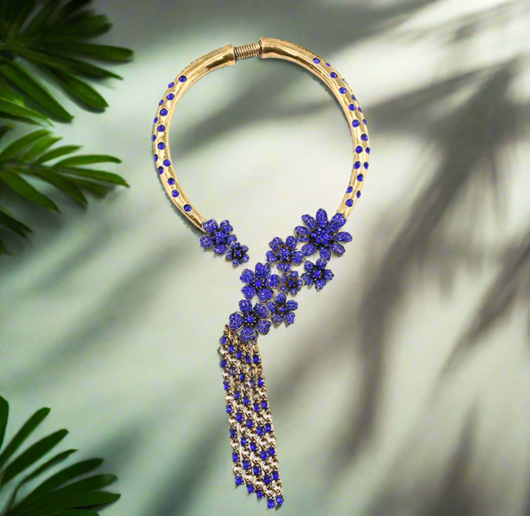 Bold vintage gold statement necklace featuring sapphire blue floral accents and cascading chain tassels, displayed on a black mannequin bust