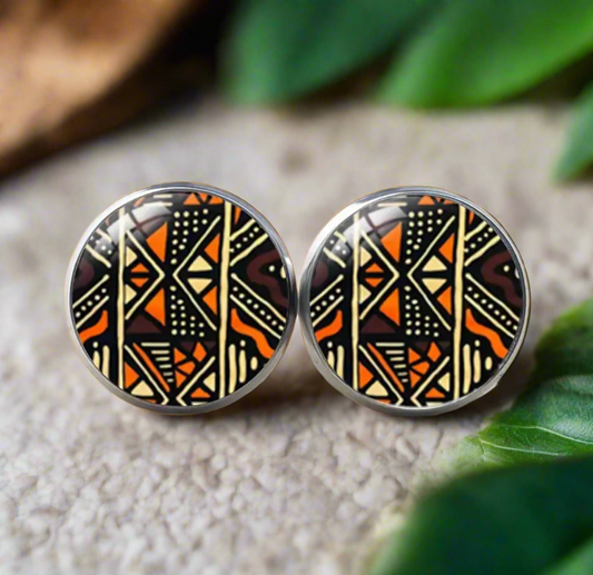 Round stud earrings featuring a bold black, white, and mustard yellow Bogolan-inspired tribal pattern with geometric and zigzag details on a glossy finish.
