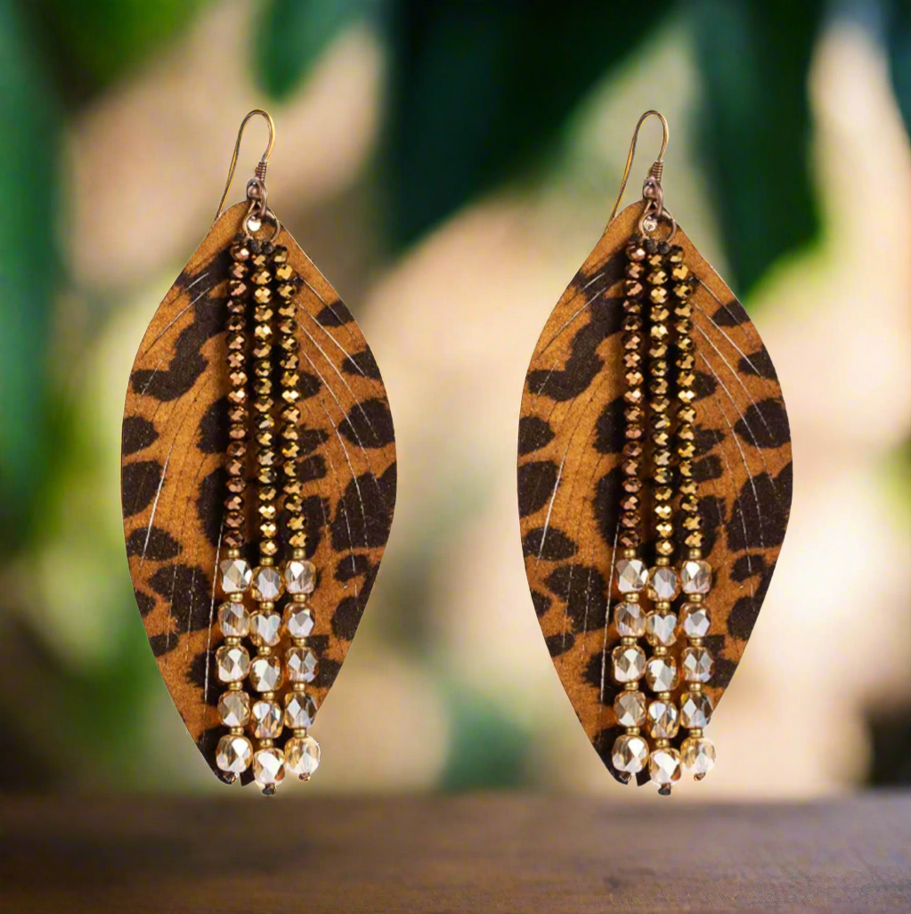 Leopard-print faux leather earrings with beaded strands of gold, bronze, and crystal beads, displayed on a white surface.