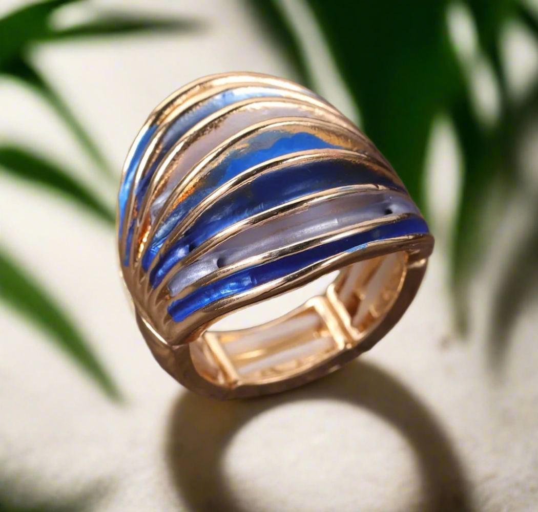 Bold gold statement ring with curved blue and pearl-toned enamel accents, placed on a wooden surface.