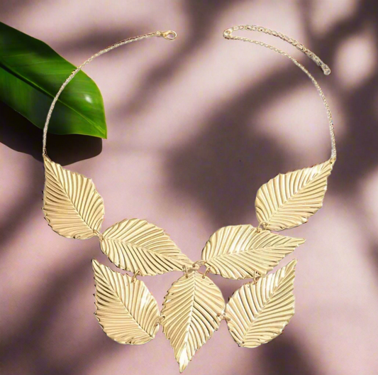 Close-up of the Gladys Golden Leaves Necklace featuring seven large, textured gold leaves arranged in a fan shape on a gold chain, displayed on a neutral background