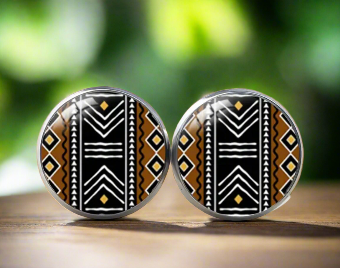 Round stud earrings featuring a bold black, white, and mustard yellow Bogolan-inspired tribal pattern with geometric and zigzag details on a glossy finish.
