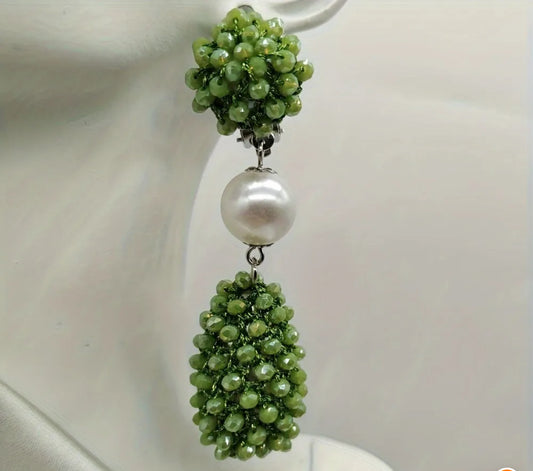 Elegant drop earring featuring clustered olive-green beads, a large faux pearl, and a teardrop bead cluster, shown on an earring stand.

