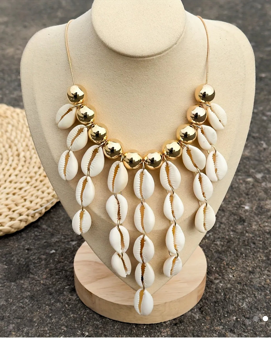 Statement necklace featuring natural white cowrie shells and shiny gold beads, displayed on a beige bust with a neutral background.