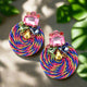 Channel vibrant island vibes with these bold, round earrings, featuring a mesmerizing swirl of braided threads and a dazzling cluster of multicolored gemstones on top. The bright pink, blue, and gold spiral creates an eye-catching centerpiece, while the sparkling crystals add a glamorous finishing touch. 