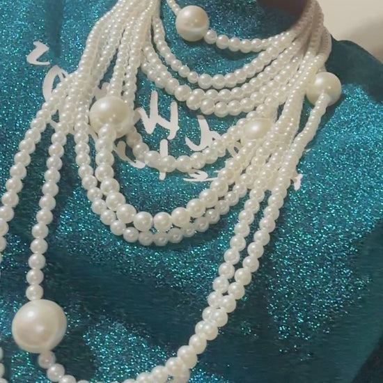 A luxurious looking  multi-layered pearl necklace displayed on a black bust stand, featuring cascading strands of white pearls in varying sizes with matching pearl drop earrings.