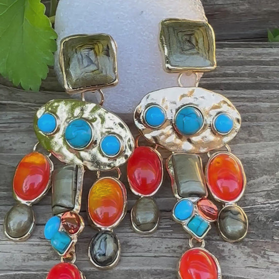 Colorful dangle earrings with gold backing, featuring orange, turquoise, and olive-green stones in various shapes and sizes arranged in a cascading design.