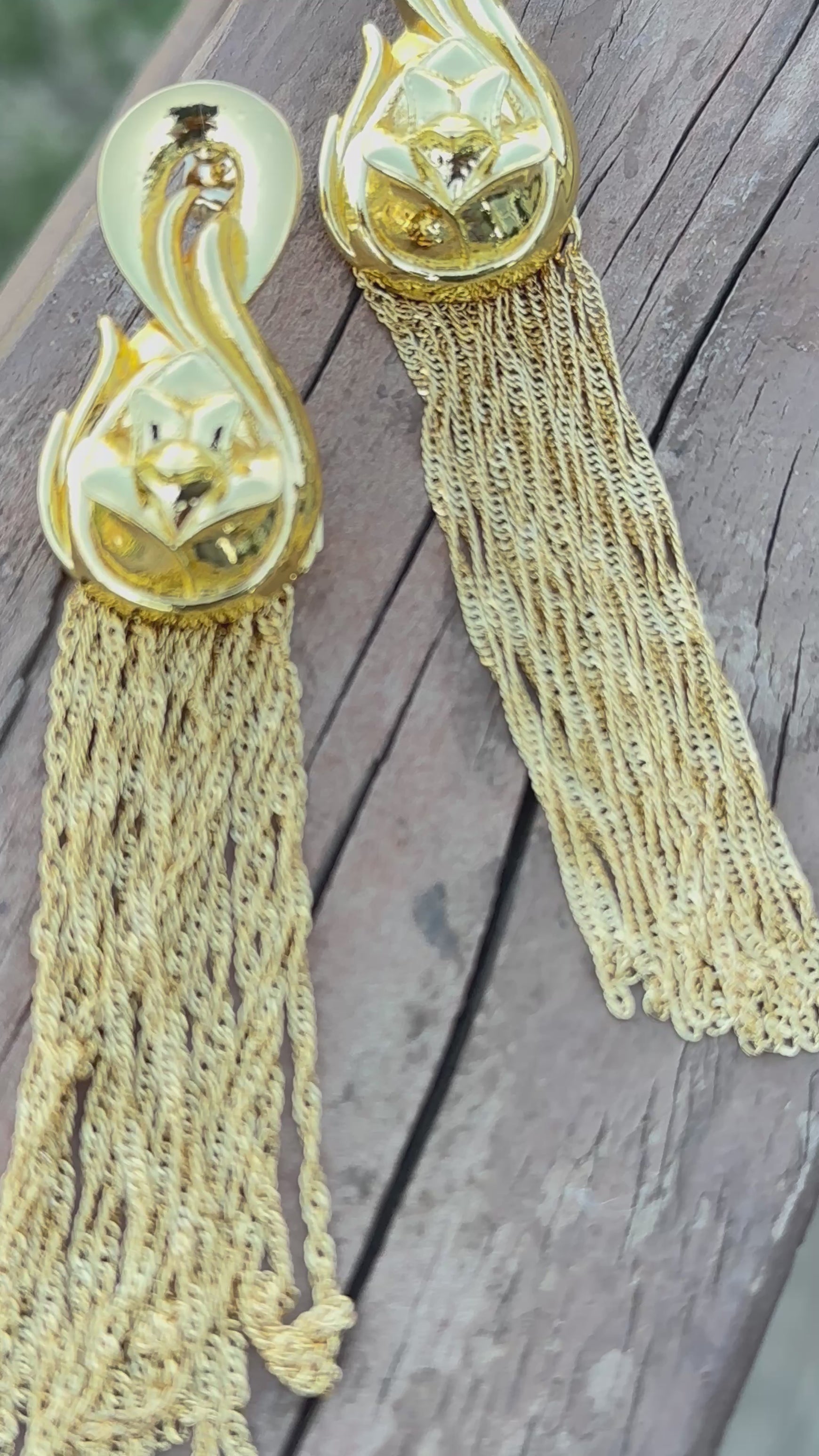 Gold Waridi tribal earrings with intricate floral design tops and long gold tassels, laid on a tropical-themed background.